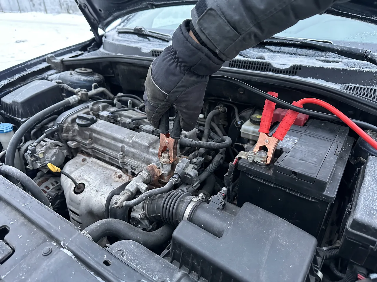 Bildmontage: minuskabeln kläms fast på en blank metalldel i motorrummet, inte på batteriets minuspol