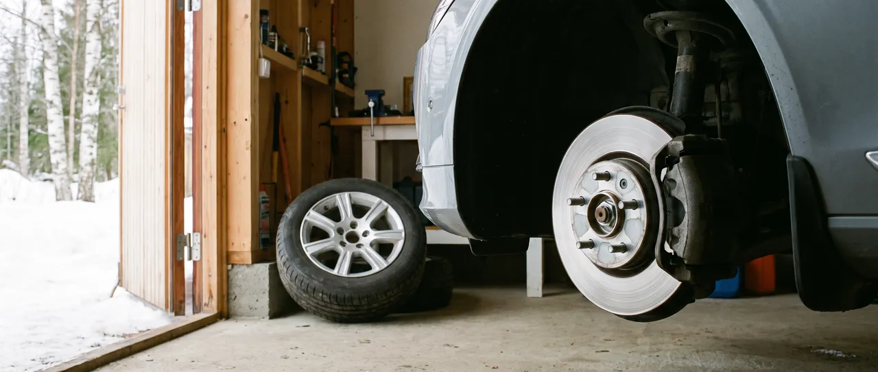 Bildmontage: en upplyft bil i garaget med navet och de fem pinnbultarna synliga, hjulet lutat mot väggen bredvid